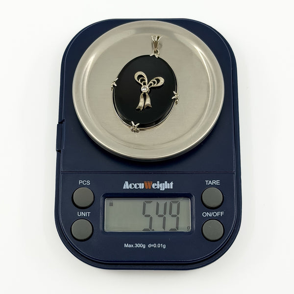 Vintage 14ct white gold black onyx and diamond bow pendant shown on scales weighing approximately 5.49g.