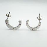 Front-facing view of sterling silver half hoop earrings set with pink sapphires and a diamond