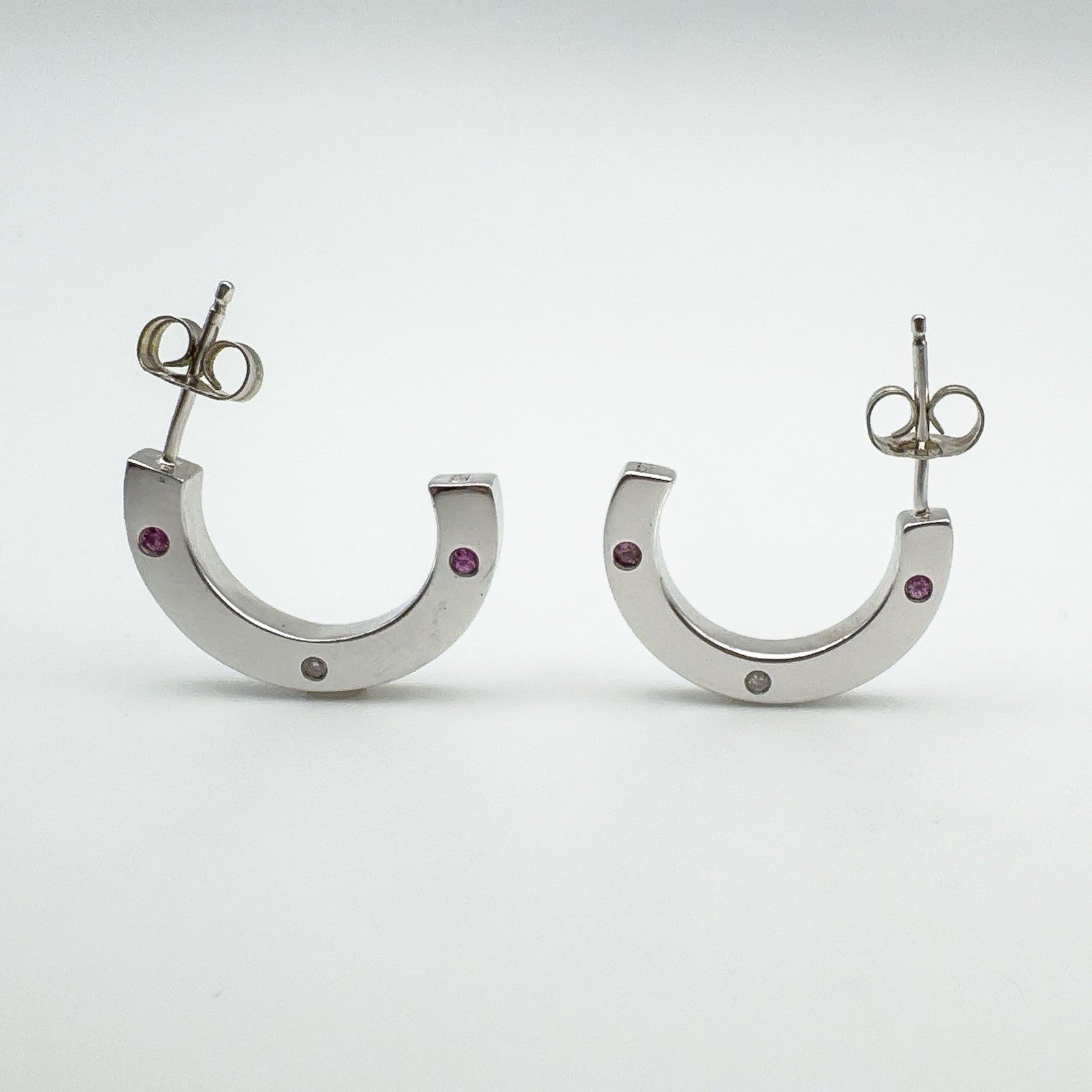 Front-facing view of sterling silver half hoop earrings set with pink sapphires and a diamond