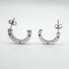 Front-facing view of sterling silver half hoop earrings set with pink sapphires and a diamond