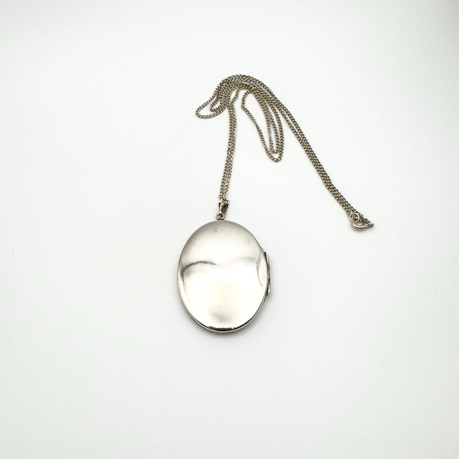 Back of silver oval locket pendant laid out with full chain