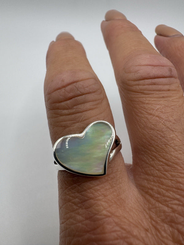 White mother of pearl heart ring shown worn on finger, natural light angle