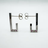 Sterling silver J hoop earrings showing pink sapphires and diamond bezel set at the base