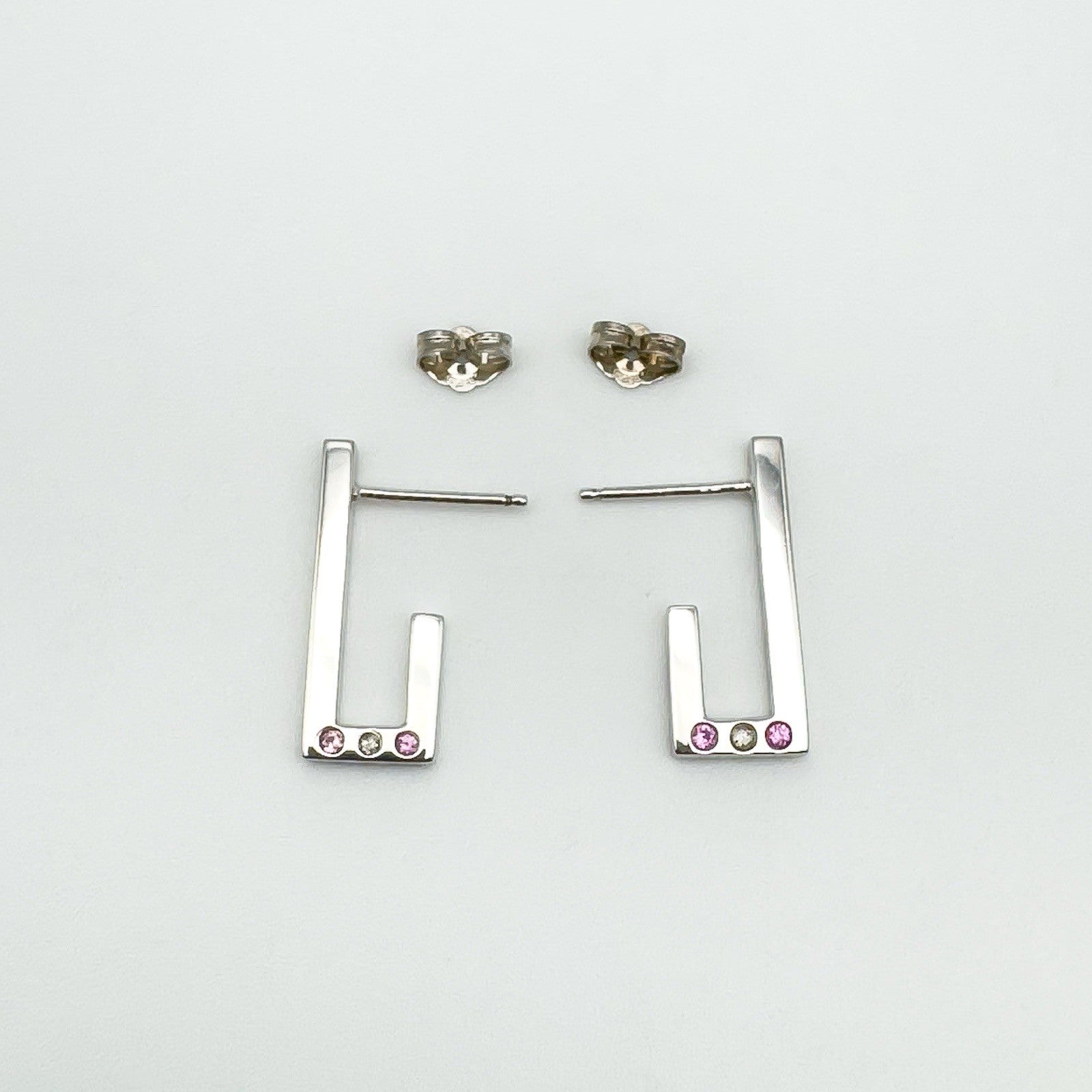Flat lay of sterling silver J half hoop earrings showing butterfly backs and gemstone settings