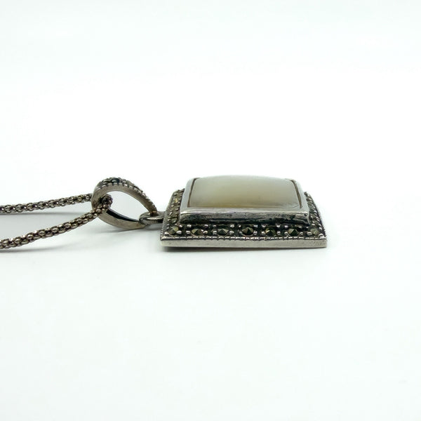 Low angle side view of the sterling silver pendant and chain, highlighting the raised square profile and finish.