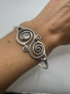 Sterling silver spiral bangle with bezel-set mother of pearl worn on wrist for scale