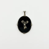 Full front view of oval black onyx and diamond bow pendant with bail and white gold frame.
