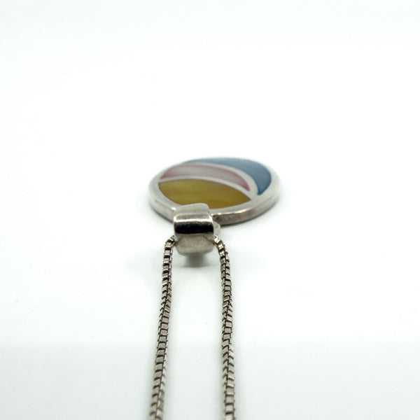 Close-up of sterling silver oval inlay pendant with smooth bail and fine box chain, multicolour inlay detail.
