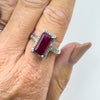 Emerald cut ruby ring with diamond halo shown on finger for scale