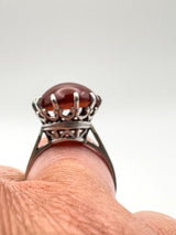 Close-up of raised carnelian solitaire ring worn on finger in silver mount