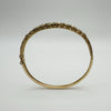 Side view of vintage gold emerald bangle with floral engraving and push clasp