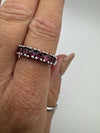 Natural light photo of sterling silver garnet ring worn on hand showing prong settings and band profile