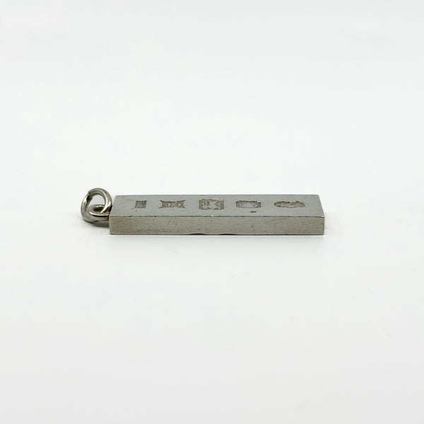 Hallmarked side of vintage sterling silver ingot pendant shown from a low angle