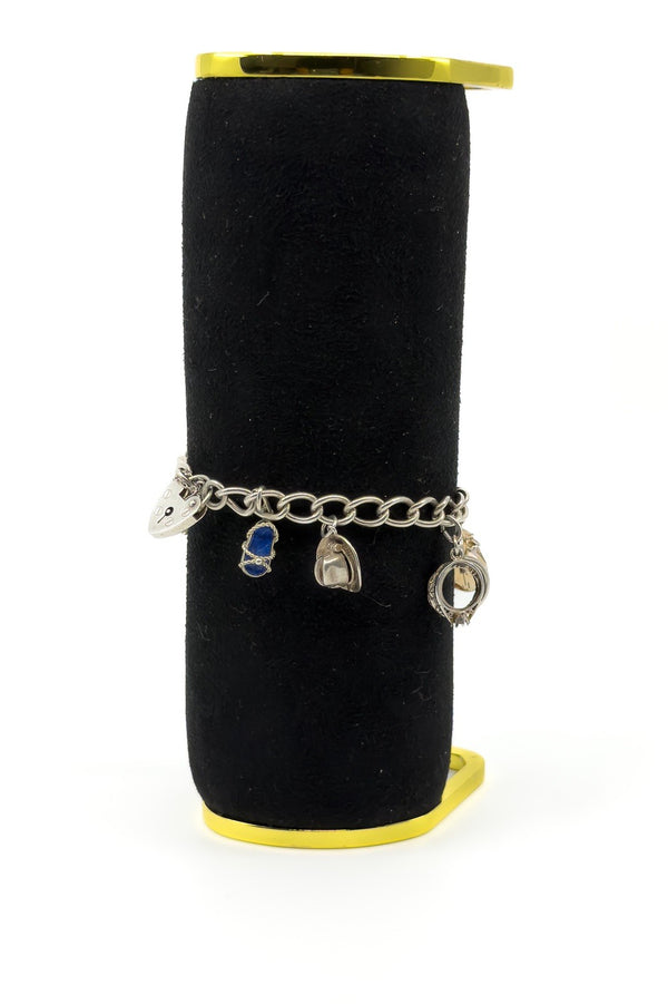Vintage sterling silver charm bracelet displayed on black stand with heart lock, lapis charm and cowboy hat charm.