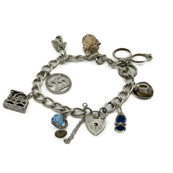 Vintage sterling silver charm bracelet with 8 charms, heart lock and safety chain on white background.