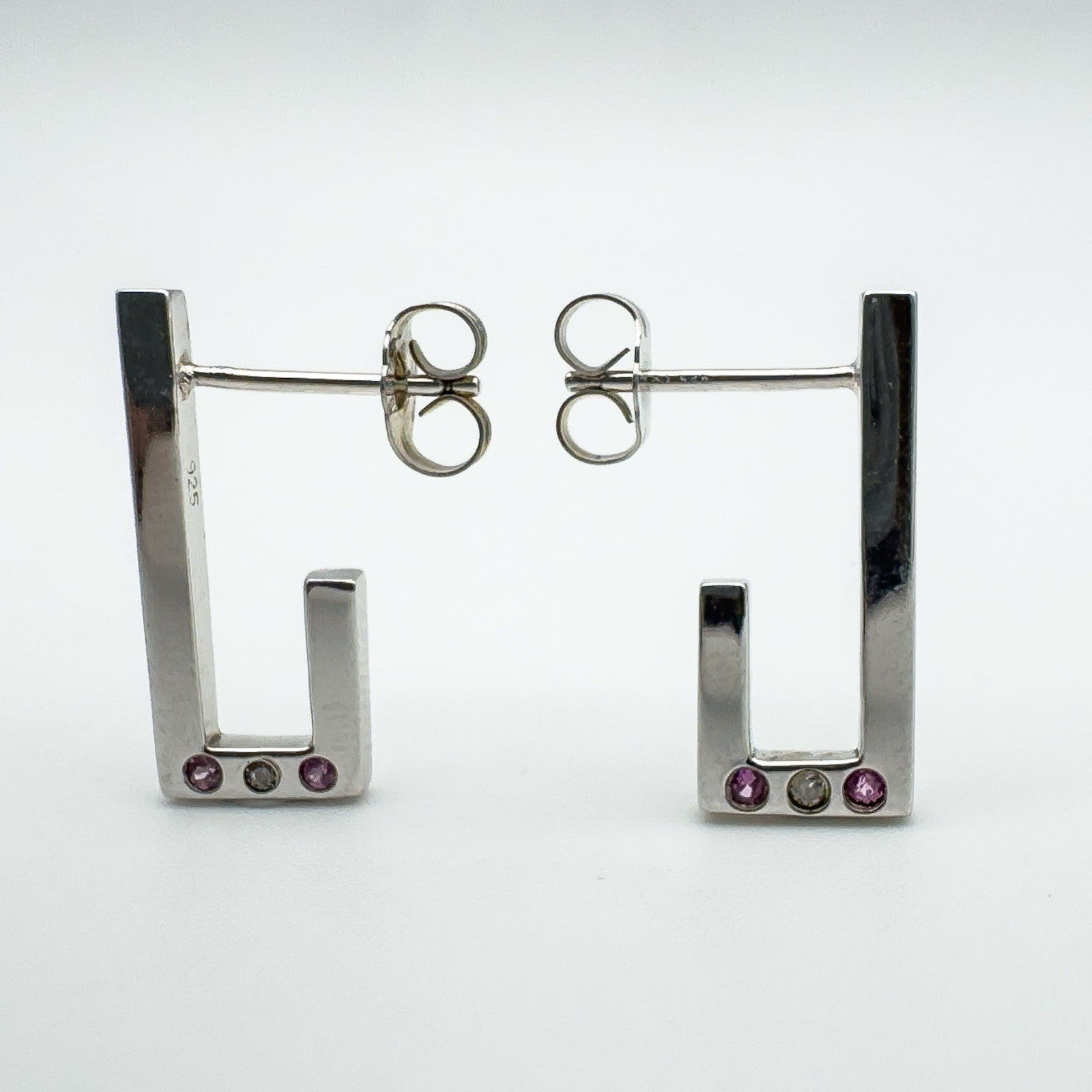 Pair of sterling silver J half hoop earrings with pink sapphires and diamond bezel set at the base