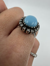 Close side detail of the raised turquoise and diamond halo ring setting worn on the hand