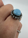 Close side detail of the raised turquoise and diamond halo ring setting worn on the hand