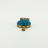 Low side view of the antique turquoise locket showing the domed gemstone setting, gold frame and bail.
