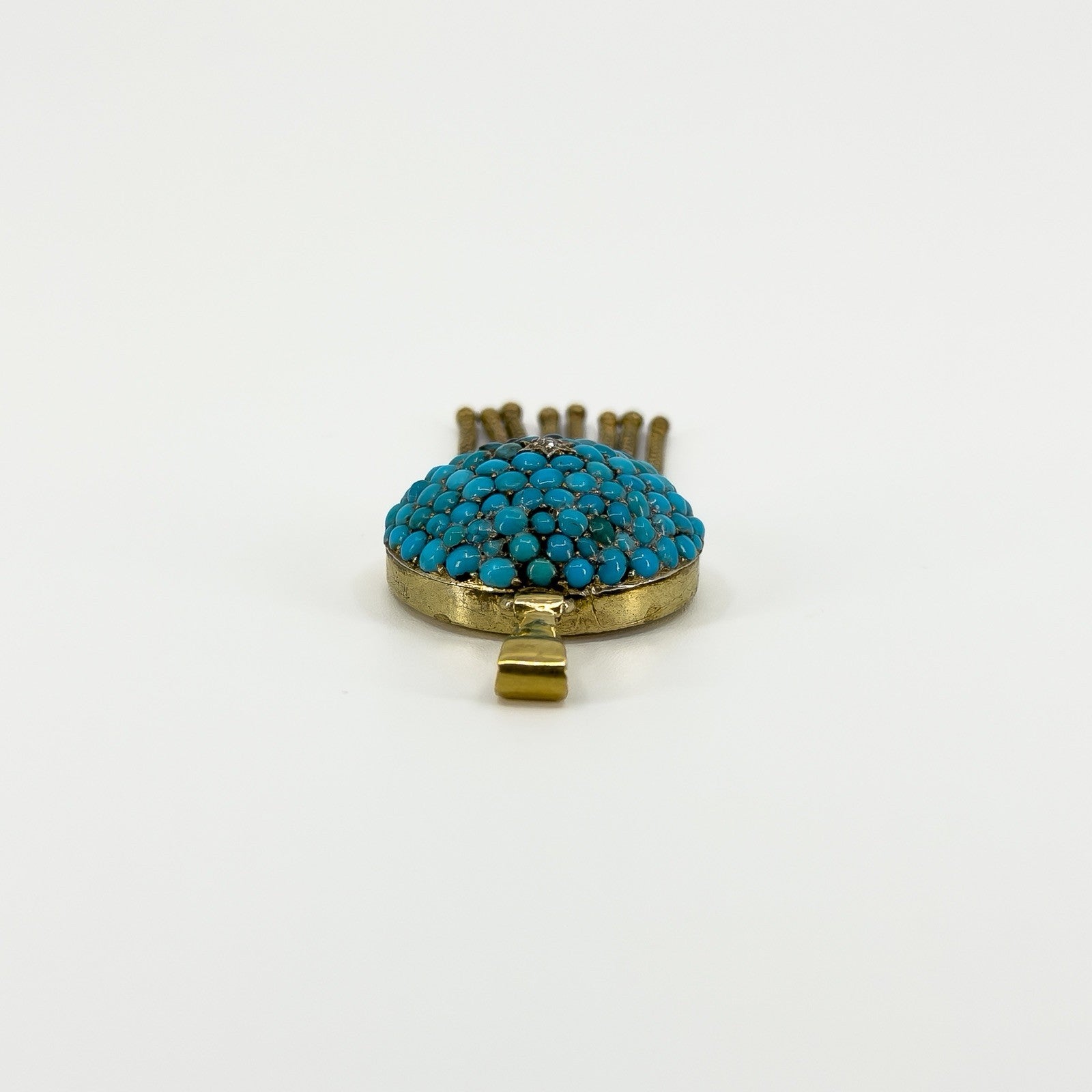 Low side view of the antique turquoise locket showing the domed gemstone setting, gold frame and bail.