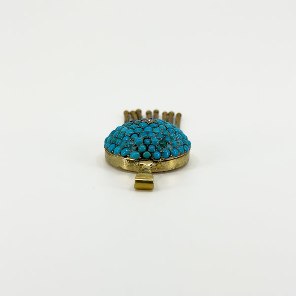 Low side view of the antique turquoise locket showing the domed gemstone setting, gold frame and bail.
