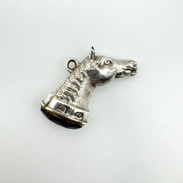 Flat lay of antique sterling silver horse head pendant set with amethyst gemstone, hallmarked Birmingham 1876