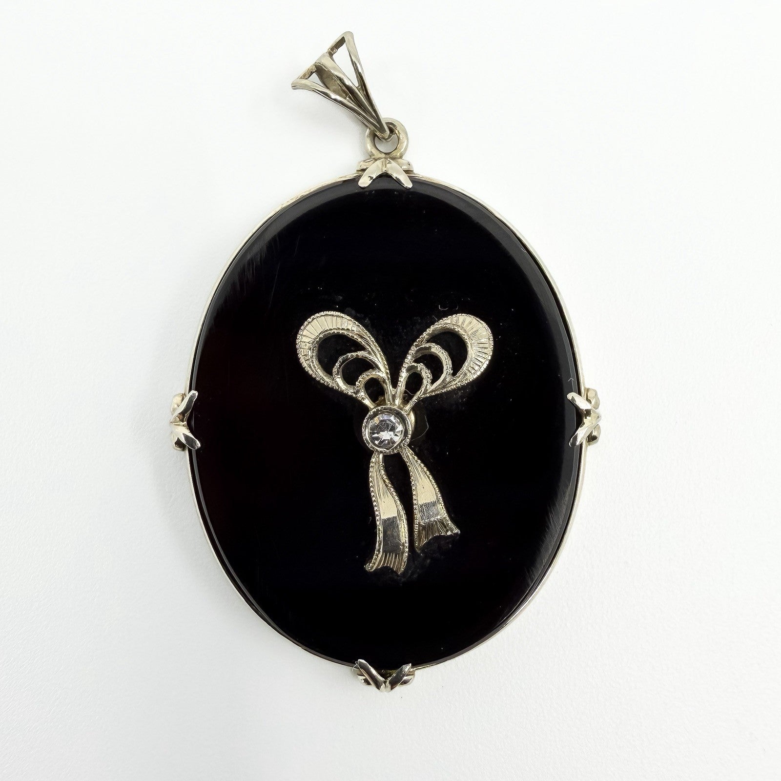 Vintage 14ct white gold black onyx bow pendant with centre diamond and bail on white background.
