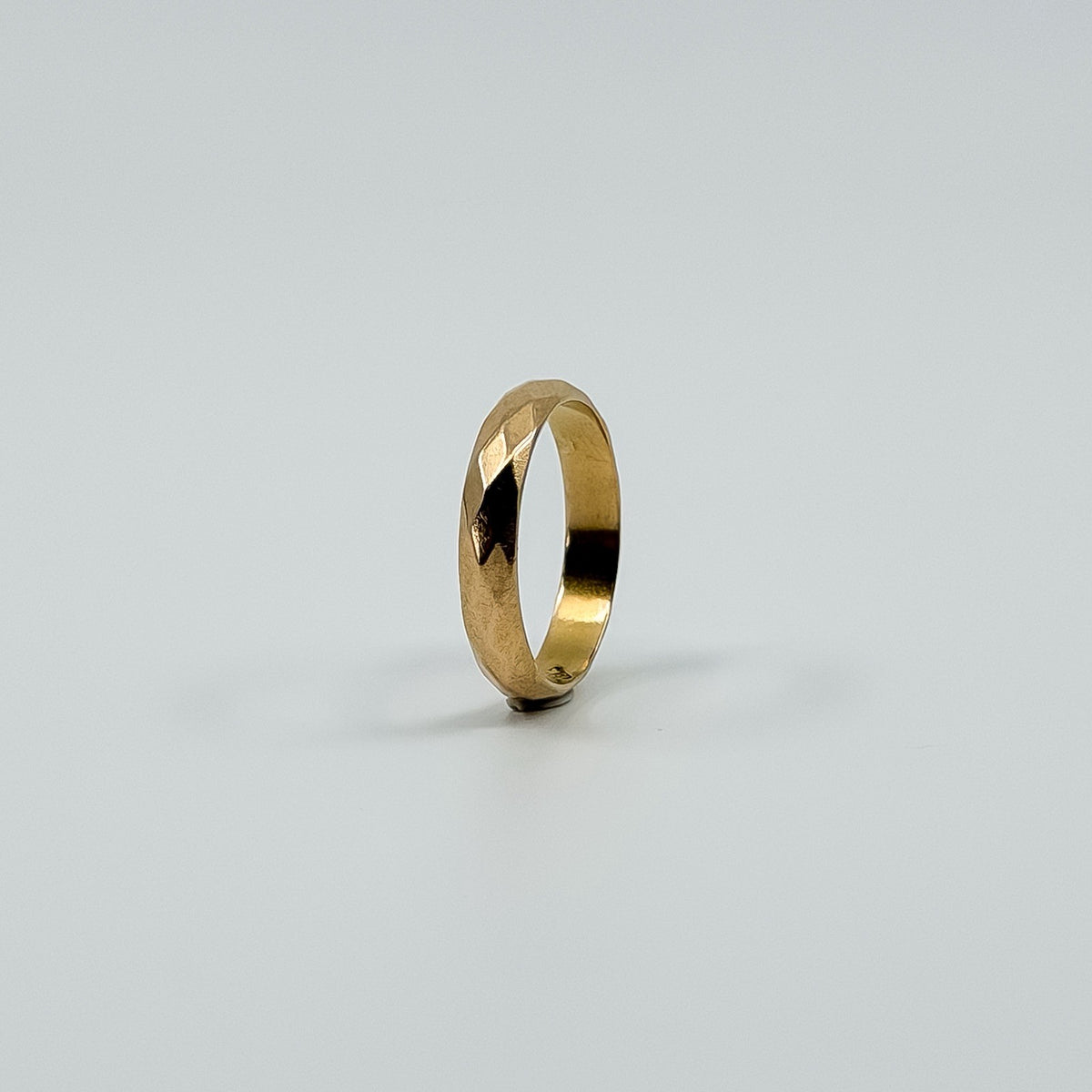 Upright angled view of vintage 18ct rose gold faceted band ring showing the slim full band shape.
