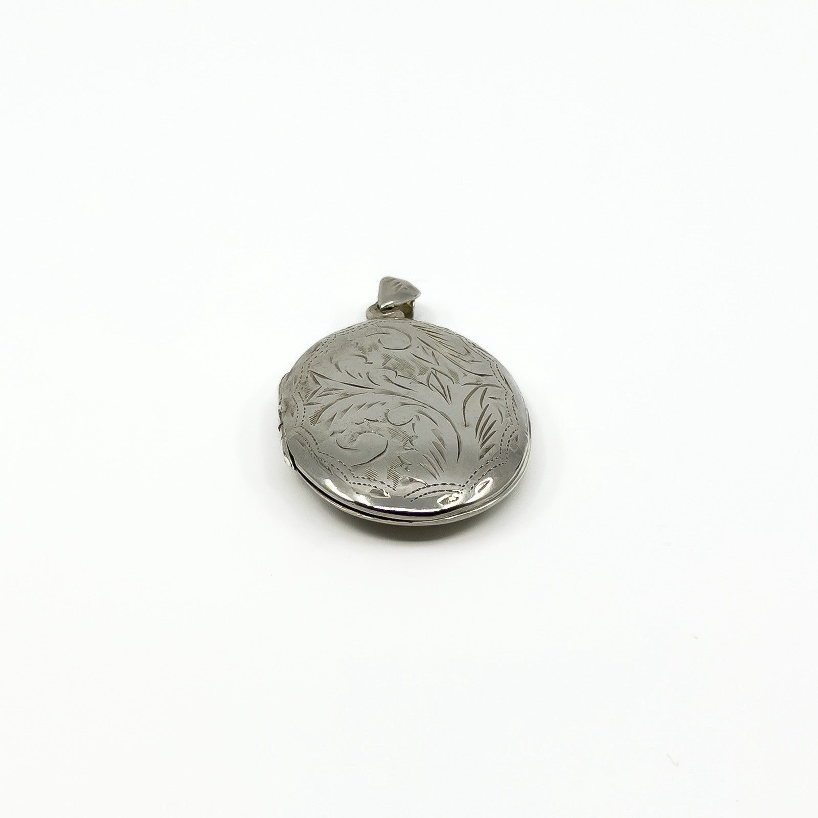 Close side view of a vintage sterling silver locket with foliate engraving