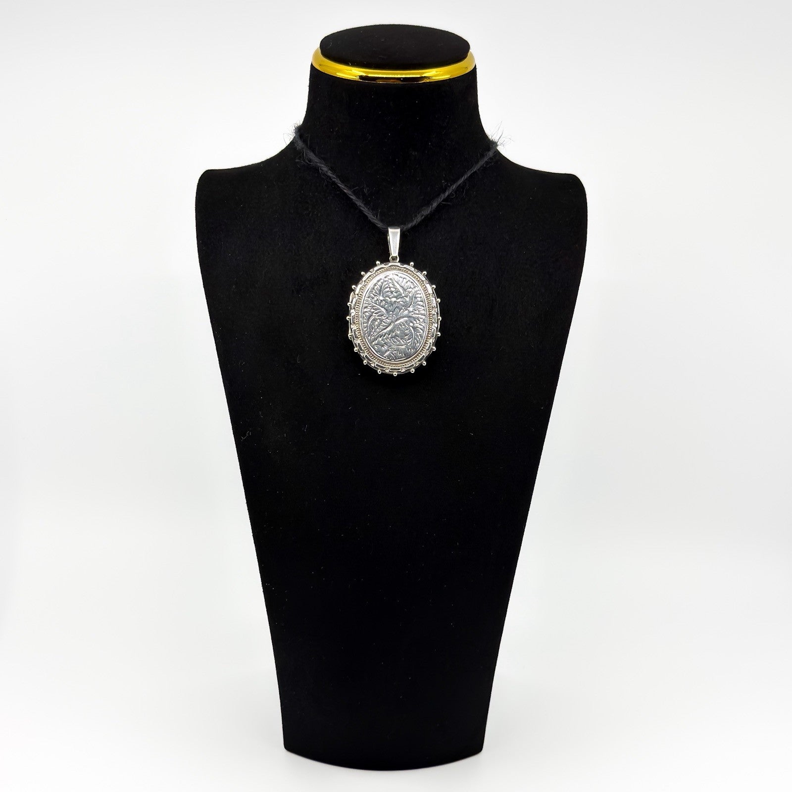 Vintage sterling silver oval locket with floral engraving shown on a black display bust