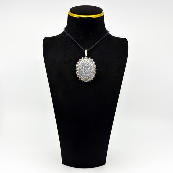 Vintage sterling silver oval locket with floral engraving shown on a black display bust
