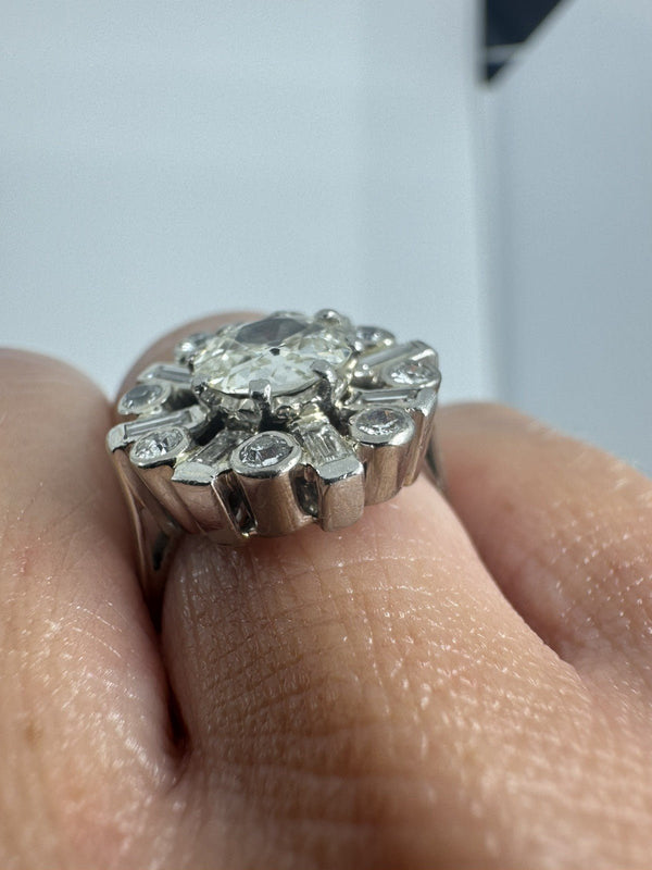 Close-up of vintage platinum diamond cluster ring worn on the hand, showing the raised old cut centre and surround.