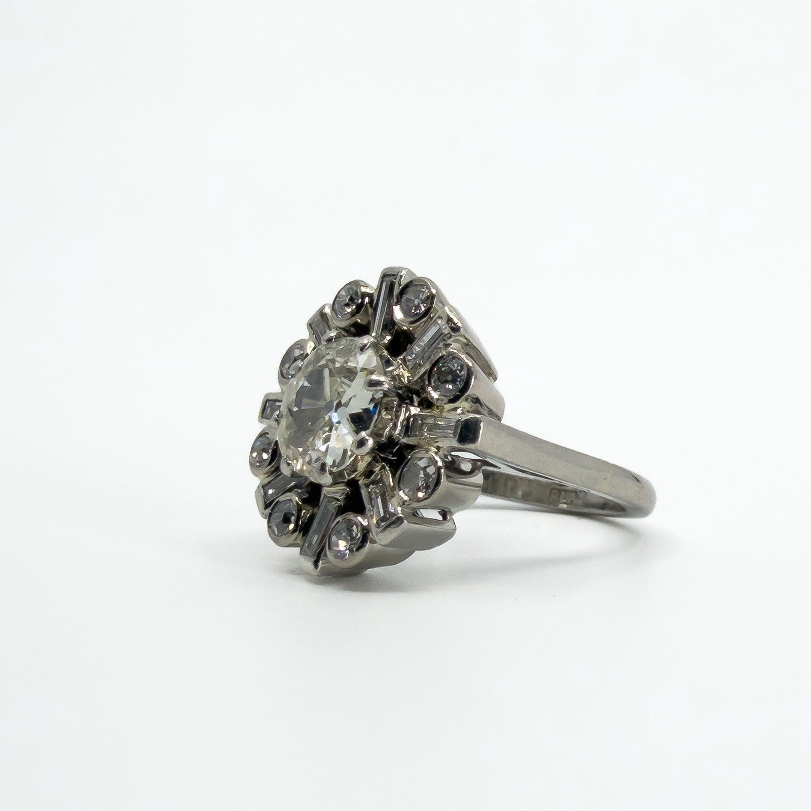 Angled front view of vintage platinum cluster ring with old cut centre and alternating round and baguette diamonds.