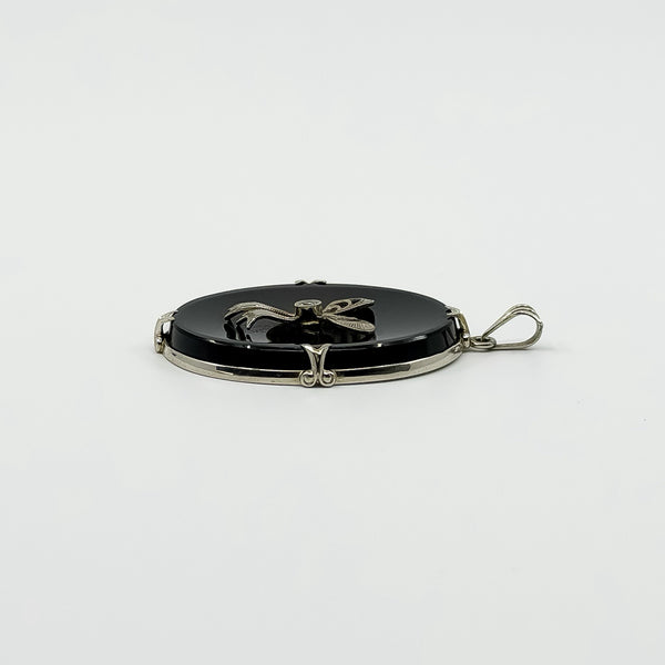 Side view of vintage black onyx bow pendant showing the white gold frame and bail.